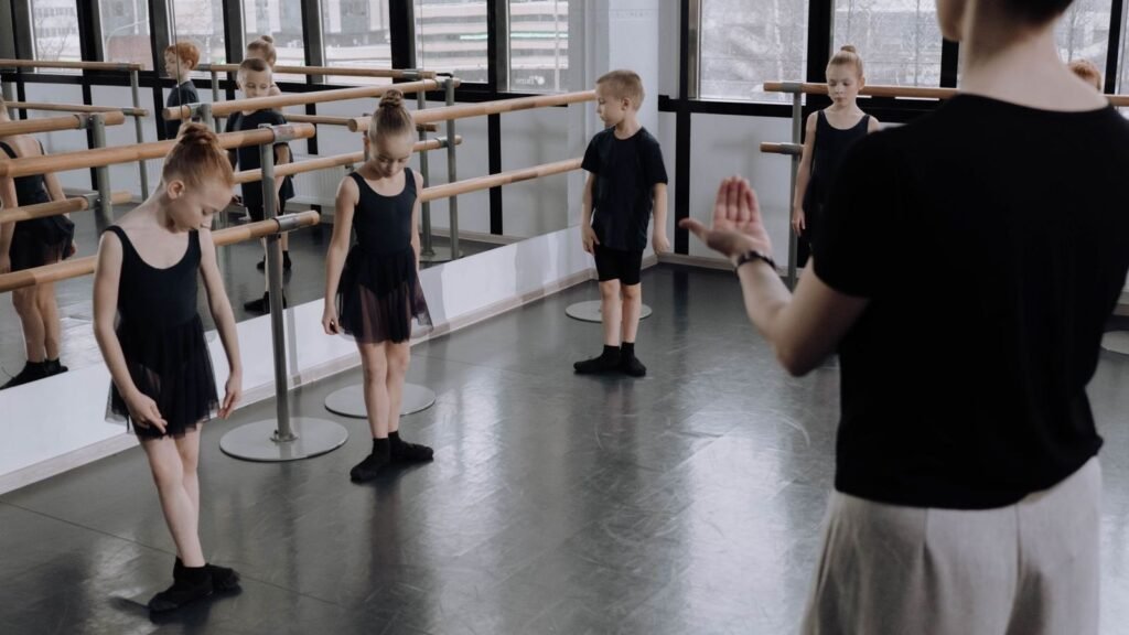 Ballet teacher leading young students at the barre in a studio