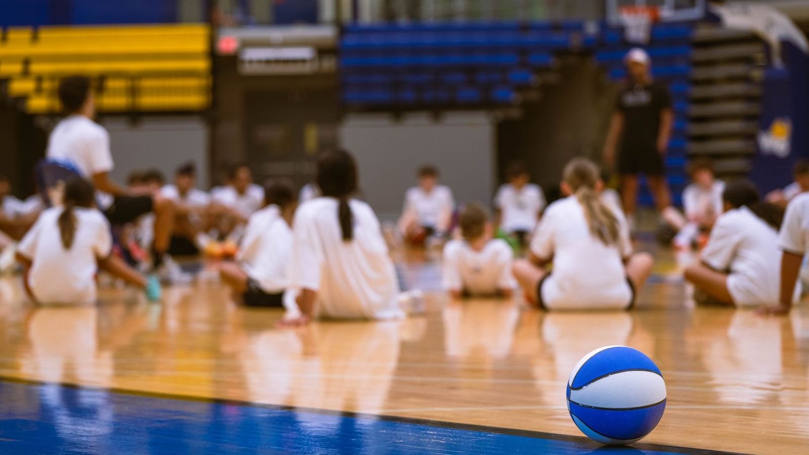 Large group of children sitting on an indoor basketball court at a holiday camp