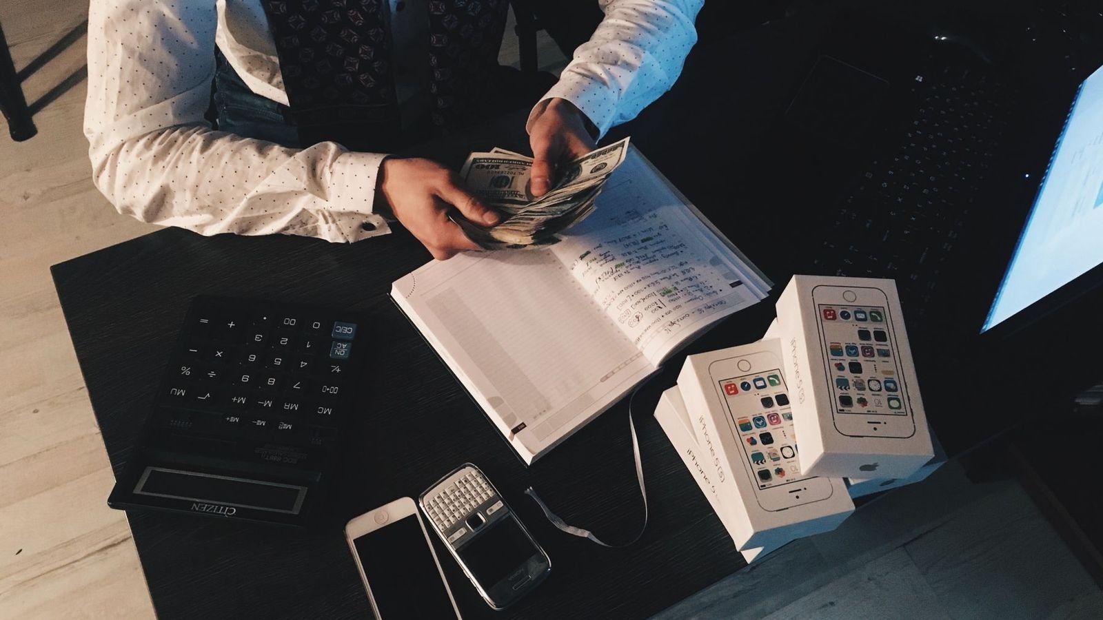 Person counting cash next to a calculator and a notebook