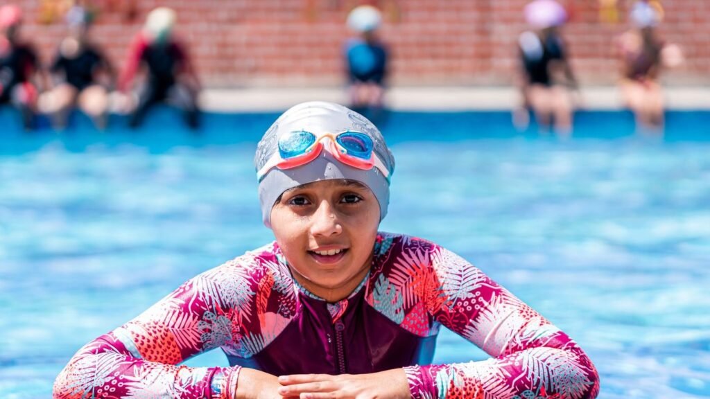 Smiling girl in a swim cap resting at the side of a pool