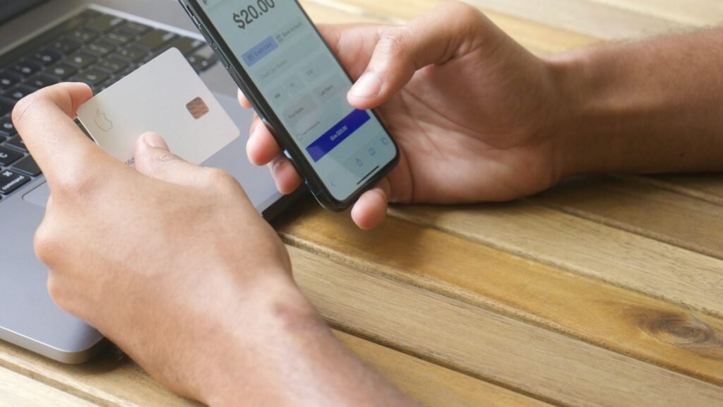 Person paying with a card on a phone next to a laptop