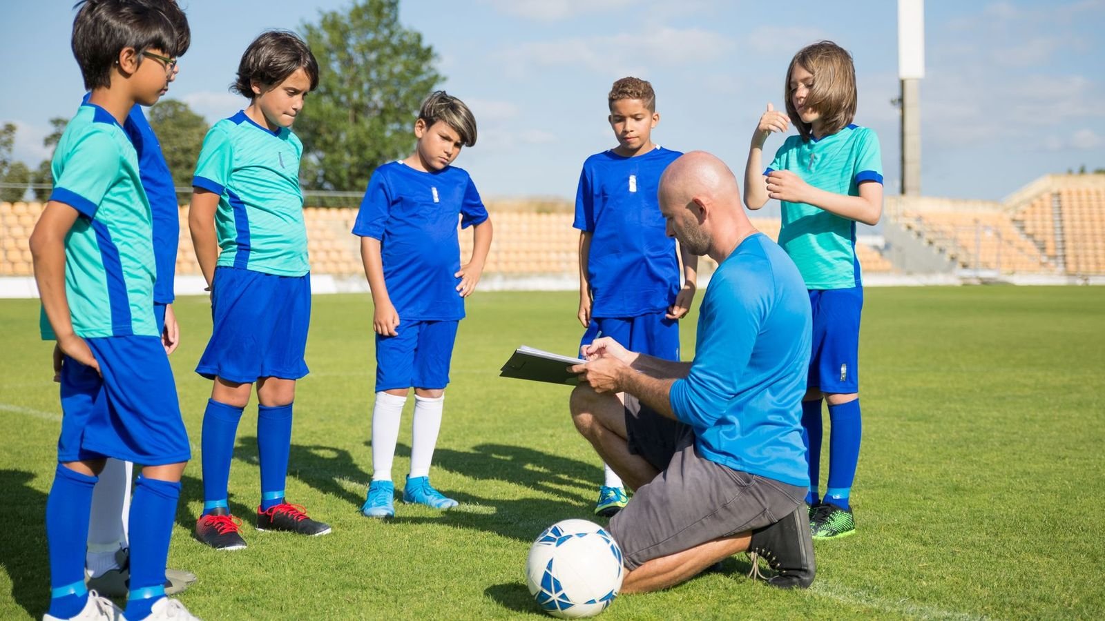 Coach kneeling to talk with a junior soccer team on a sunny field
